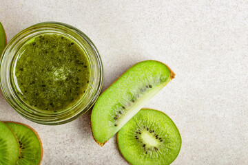 Homemade kiwi jam in a jar and kiwi slyces on concrete background with copy space