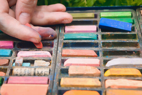 closeup of caucasian hands taking a chalk from a box of colored chalks.