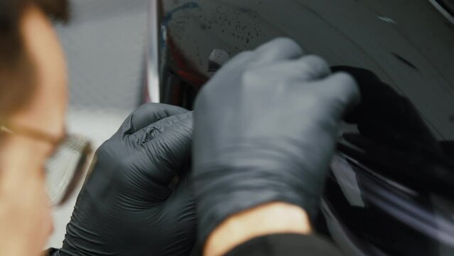 A professional puts protection on the black car body. Precise operation. Extreme close-up shot. High quality 4k footage