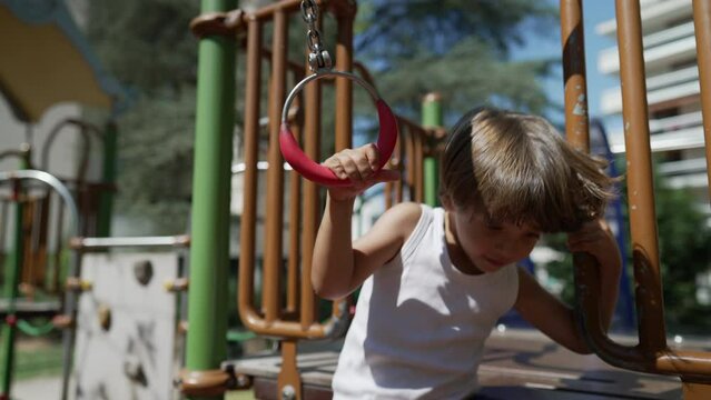 Small boy holding into monkey bar at playground structure. Active kid exercising outdoors in sunny day