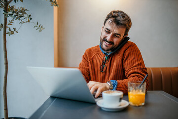 Handsome Caucasian man using a phone in the cafe and working on the laptop. Freelancer. Online work concept