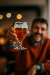 A cheerful casual dressed man sitting alone in the venue and having a drink, beer.