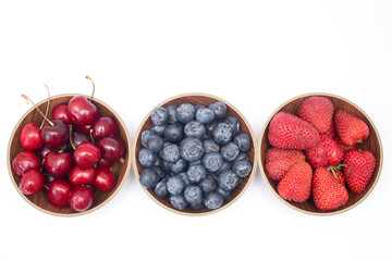 Blueberries, strawberries and cherry in bowls on white