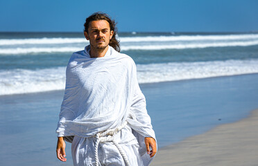 Bearded, handsome man in white robe (resembles Christ) walking next to sea