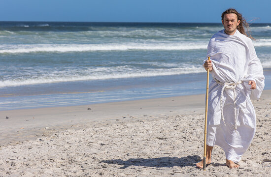 Handsome bearded man in white robe, (portrait) with staff walks next to sea