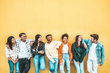 Happy multiracial friends standing over isolated background - Cheerful young people socializing outdoors - University students laughing together on yellow wall - Youth culture and friendship concept - obrazy, fototapety, plakaty