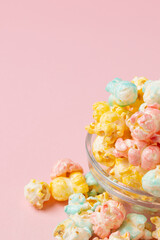 Colored glazed popcorn poured out of glass plate on a pink background hight angle with copy space