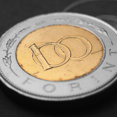 Hungarian coin of 100 forints lies on dark black surface close-up. Money of Hungary. News about economy or finance. Loan and credit. Savings and interest. Magyar forint. Square illustration. Macro