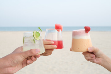 Group of happy friends hand cheering with tropical cocktails at beach party. Young people having fun on summer holiday vacation. Youth and summer vacation concept.