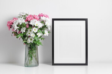Blank portrait frame mockup with fresh flowers bouquet in white room interior