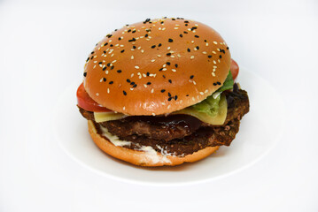 Double meat burger with vegetables on a white background. Delicious cheeseburger on a plate. Meat fast food. A large hamburger with a double cutlet.