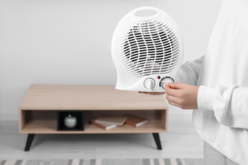 Woman turning on electric fan heater at home, closeup. Space for text