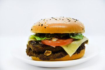 Double meat burger with vegetables on a white background. Delicious cheeseburger on a plate. Meat fast food. A large hamburger with a double cutlet.