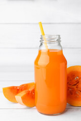 Tasty pumpkin juice in glass bottle and cut pumpkin on white wooden table