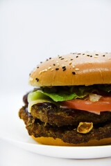 Double meat burger with vegetables on a white background. Delicious cheeseburger on a plate. Meat fast food. A large hamburger with a double cutlet.