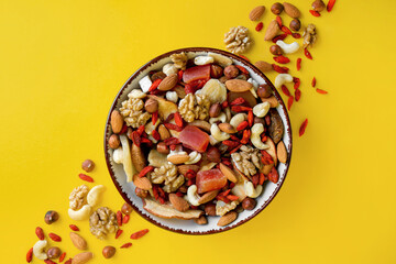 Bowl with mixed dried fruits and nuts on yellow background, flat lay