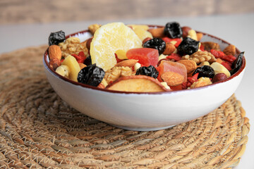 Bowl with mixed dried fruits and nuts on wicker mat, closeup