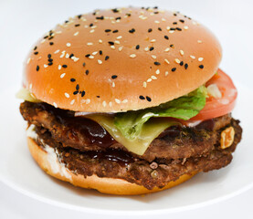 Double meat burger with vegetables on a white background. Delicious cheeseburger on a plate. Meat fast food. A large hamburger with a double cutlet.