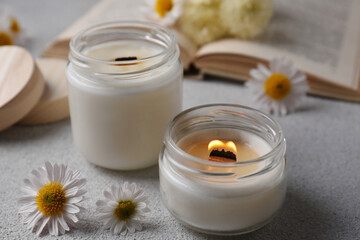 Fototapeta na wymiar Burning scented candles and chamomile flowers on light gray textured table, closeup