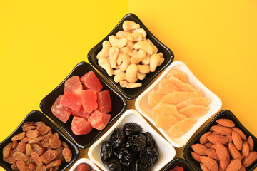 Bowls with dried fruits and nuts on yellow background, flat lay