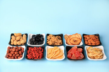 Bowls with dried fruits and nuts on light blue background, space for text