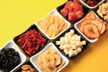 Bowls with dried fruits and nuts on yellow background, above view