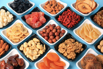 Bowls with dried fruits and nuts on light blue background
