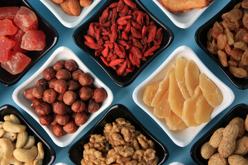 Bowls with dried fruits and nuts on light blue background, flat lay