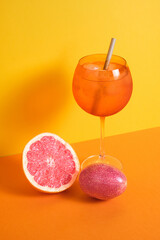 cocktail glass with ice and straw accompanied with passion fruit and grapefruit on orange and yellow minimalistic background