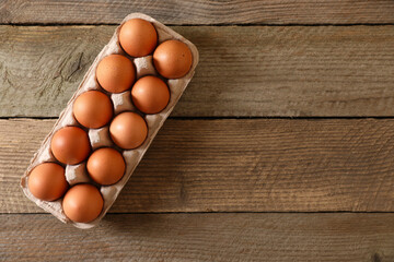 Fresh raw chicken eggs in carton on wooden table, top view. Space for text