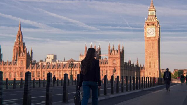 Attractive European looking woman walking on Westminster Bridge London with smiling, smirking face. Stylish trendy businesswoman having a walk on Westminster Bridge on a morning crowded day