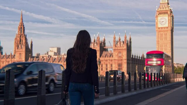 Attractive European looking woman walking on Westminster Bridge London with smiling, smirking face. Stylish trendy businesswoman having a walk on Westminster Bridge on a morning crowded day