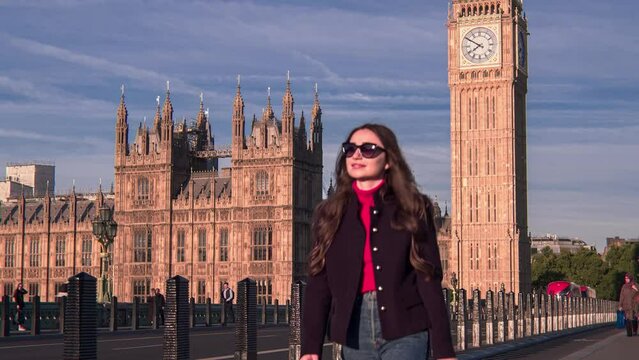 Attractive European looking woman walking on Westminster Bridge London with smiling, smirking face. Stylish trendy businesswoman having a walk on Westminster Bridge on a morning crowded day
