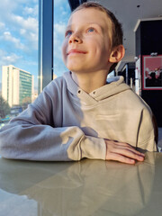 Cute 8 years old boy enjoy sitting near window and  looking through the window