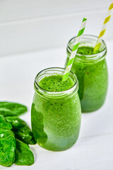  Top view of glasses jars with straws filled with green smoothie and spinach on the wooden table
