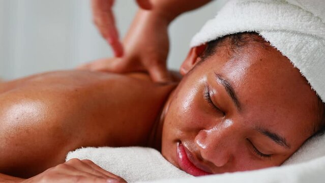 Back spa massage. Beautiful African American woman getting massage in beauty spa and wellness center. Facial treatment and skin care concept.