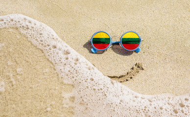 Sunglasses with flag of Lithuania on a sandy beach. Nearby is a sea lightning and a painted smile. Travel and vacation concept for Lithuanians
