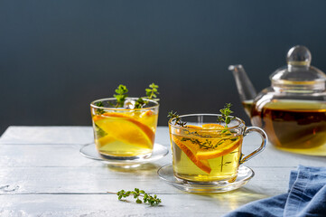 Herbal tea with oregano and thyme and slices of orange in glass cups and teapot with blue background