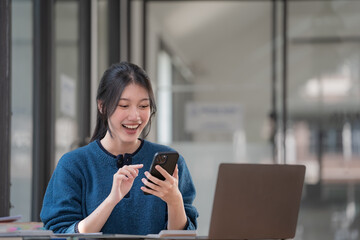 Asian woman looking at her smartphone, cheering and celebrating while receiving good news.