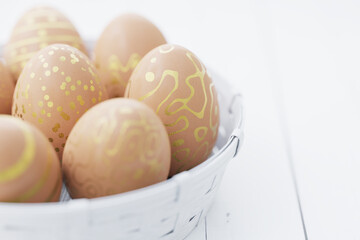 Easter eggs in brown color with a golden pattern in a white basket on a white wooden table. Easter still life. 3d render.