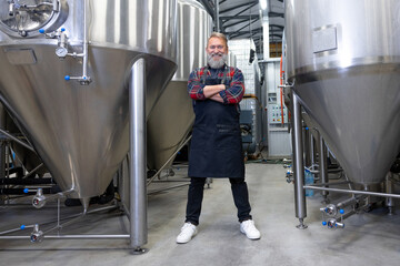 Brewery worker standing near the metal tanks and looking determined