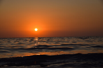 Vibrant sunset descending on the horizon, sea in golden colors, small waves gently touching the...