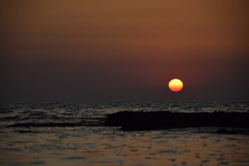 Vibrant sunset descending on the horizon, sea in golden colors, small waves gently touching the sands,