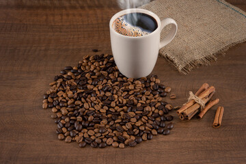 Coffee beans standing on wooden floor and hot coffee in mug,