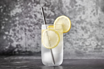 Glass of water with ice and lemon, metal straw on a concrete gray background. © Alex