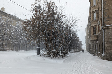 Snowfall in the old city. A lonely man walks along a winter street among snowdrifts during a snowfall. Weather forecast.
