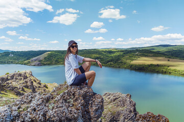 Naklejka na ściany i meble Young traveler woman sitting on a rocks above blue lake .Traveling in the summer nature in Bulgaria . Pchelina Lake 