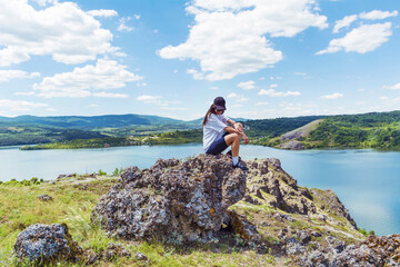 Obraz premium Young traveler woman sitting on a rocks above blue lake .Traveling in the summer nature in Bulgaria . Pchelina Lake 