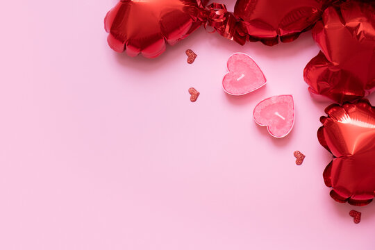 Valentines Day background with copy space and two candels with red heart shape balloons on pink background
