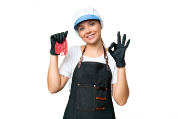 Butcher woman wearing an apron and serving fresh cut meat over isolated chroma key background showing ok sign with fingers